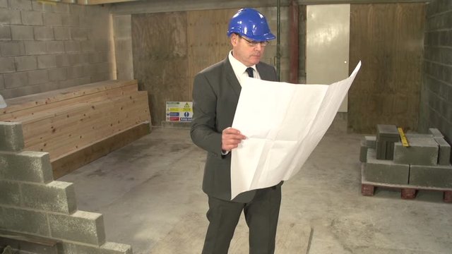 Man on Construction / Building Site looking through the plans / Blueprints. Could be a Builder, Architect or Inspector. Crane Shot. Stock Video Clip Footage