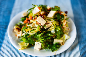 Green salad with feta pieces, onion, leek and sesame seeds on white plate.