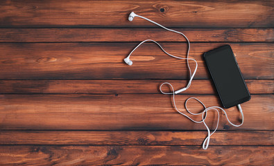 Black smartphone and white headphone lies on a wooden background. Top view, copy space. Music concept.