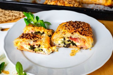 Sliced baked puff pastry bun with ham, cheese and olive on plate and on baking tray.