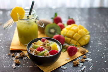 gesundes Frühstück: Joghurt mit Crunchys, frischen Erdbeeren, Kiwis, Mangos und Kokosflocken mit. Dazu ein grüner Smoothie im Einmachglas