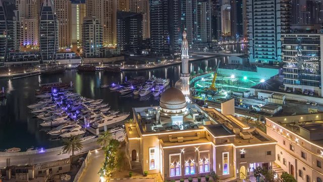 Yachts in Dubai Marina flanked by the Al Rahim Mosque and residential towers and skyscrapers aerial night to day transition timelapse. Modern high rise skyline with boats and wooden dhows