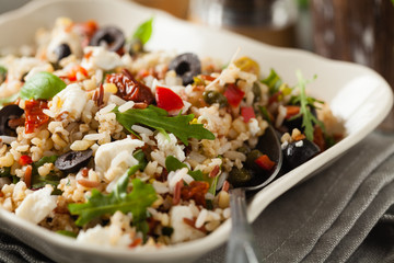 Trendy lunch with red rice, a mix of groats and vegetables. Front view. Served in white bowl on grey wooden background.