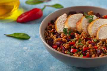 Trendy lunch with cereal, beetroot and chicken. Served in a bowl on a blue painted background. Front view.