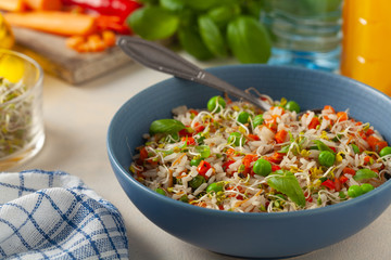 Trendy lunch with rice and vegetables. Served in a blue bowl, on a bright painted background. Front view.