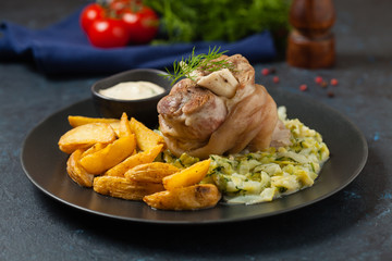 Boiled knuckle, served with cabbage and baked potatoes. Front view. Darkblue background. Dark mod.