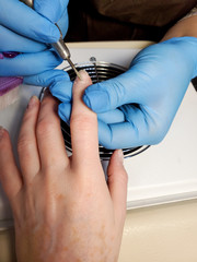 Shot of a master in rubber gloves applying an electric nail file to remove cuticles in a beauty salon.