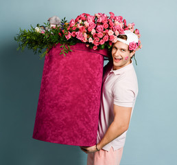 Young man with a seductive smile delivery guy with a kiss on a cheek is carrying huge box with flowers for birthday