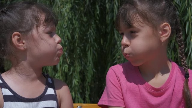 Funny little sisters play together. The cheerful little girls puffed out their cheeks.