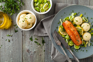 Portion of fried salmon, served with mashed potatoes and cooked leek. Top view. Gray plate, wooden background.