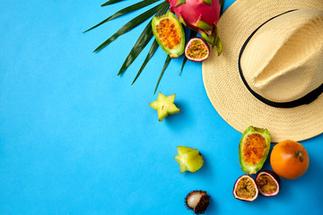 Fototapeta na wymiar summer holidays, vacation and travel concept - close up of straw hat and exotic fruits on blue background