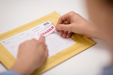 delivery, mail service, people and shipment concept - close up of woman's hands sticking fragile...