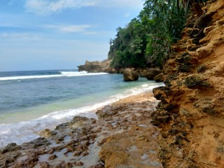 Fototapeta premium Beach with rocks, waves and blue sky. The beautiful Sanggar beach in Tulung Agung, East Java, Indonesia.