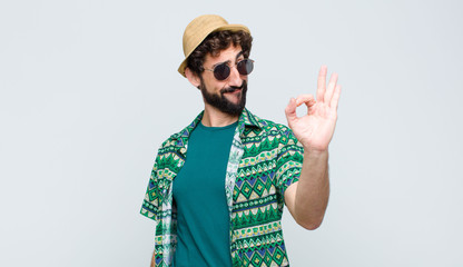 young tourist man feeling happy, relaxed and satisfied, showing approval with okay gesture, smiling against white wall