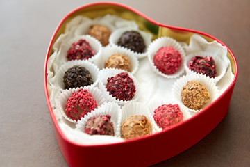 sweets, confectionery and food concept - candies in red heart shaped chocolate box on brown background