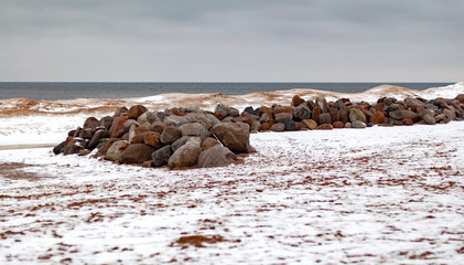 A ridge of large boulder stones on the beach on the shore of Lake Ladoga on a winter cloudy day