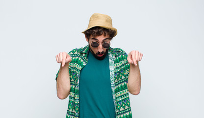 young tourist man with open mouth pointing downwards with both hands, looking shocked, amazed and...
