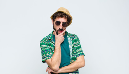 young tourist man with mouth and eyes wide open and hand on chin, feeling unpleasantly shocked,...