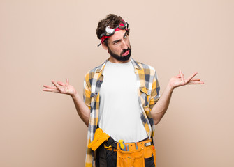 young housekeeper man shrugging with a dumb, crazy, confused, puzzled expression, feeling annoyed...