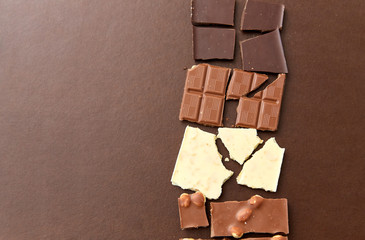 sweets, confectionery and food concept - milk, dark and white chocolate bars on brown background