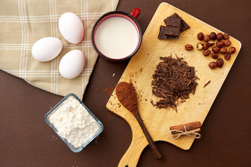 confectionery and culinary concept - chocolate, cocoa powder, hazelnuts with milk, eggs and flour on brown background