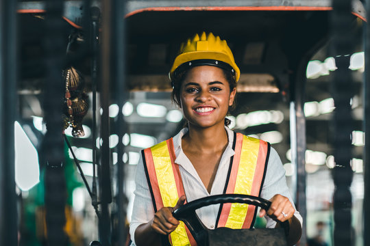 Women labor worker at forklift driver position with safety suit and helmet happy smile enjoy working in industry factory logistic shipping warehouse.