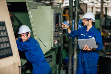 Machine service team checking CNC and re-programming process during factory production.