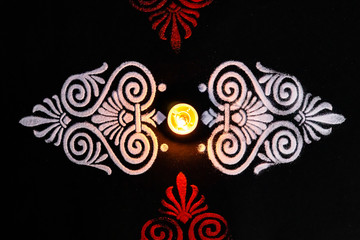 top view of beautiful shining diya and white red rangoli art on black background. deepwali and dhanteras concept