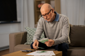 finances, savings and people concept - senior man with calculator and bills counting money at home in evening