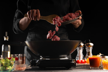 Cooking, the chef fries fresh pork meat in a pan, against a background of vegetables. Freezing in motion. Cooking. Recipe book, cooking and gastronomy.