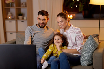 family, leisure and people concept - happy smiling father, mother and little daughter watching tv at home at night