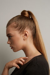 A blonde European girl with long straight hair in a high ponytail and a hair knot is posing on the...