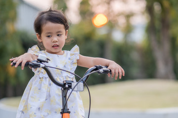 Fototapeta na wymiar Yellow dressed beautiful little girl riding bicycle at park.