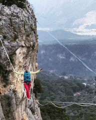 A woman is walking along a stretched sling. Highline in the mountains. Woman catches balance. Performance of a tightrope walker in nature.
