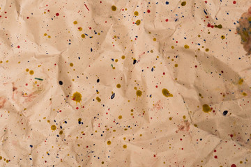 Drops of watercolor paint on yellow rumpled paper background.