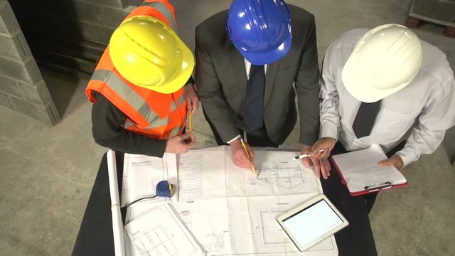 Meeting on Construction / Building Site with a Builder, Architect & Inspector. They are looking through the plans on a Digital Tablet. Overhead, Aerial view Stock Video Clip Footage