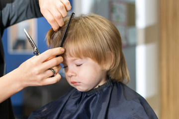 hairdresser's hands with scissors and a comb cut a small child, focus on the hands, the child in blur. hairdressing services for children