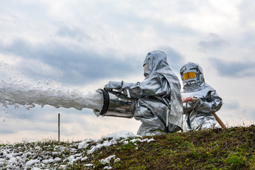 Two firefighters in high-temperature protective suits during an exercise extinguish a fire with a wide stream.
