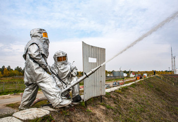 Two firefighters in high-temperature protective suits during an exercise extinguish a fire with a...