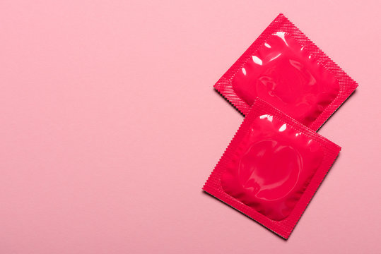 Two condoms in closed foil packaging on pink pastel background with copy-space.