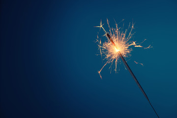 Bengal fire sparkler burning with sparks on blue background