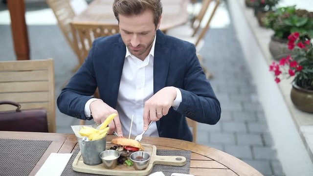 young man eating a burger with fork and knife at a terace
