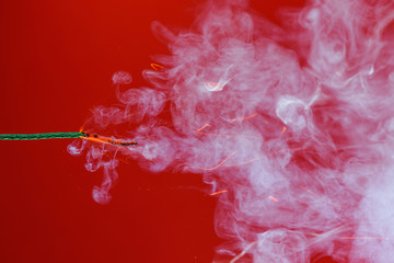 Burning fuse wick dynamite of fireworks cord with sparks and smoke on red background