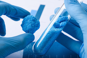 Researcher show blue crystal material in hand and glass test tube in laboratory