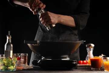 Cooking dishes by the chef, frying fresh pork meat in a pan, pepper. Freezing in motion, on the background of vegetables. Gastronomy and cooking. Cooking food