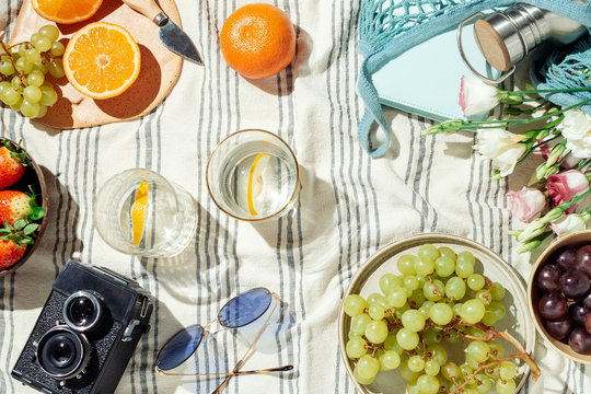 Feminine summer picnic flatlay, fruits, berries and lemon water on striped cotton blanket