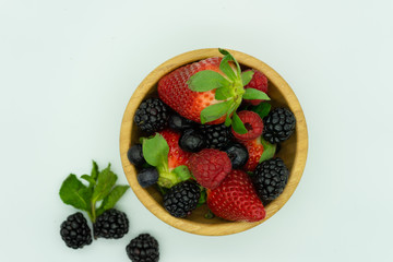 Top view of wooden bowl full of strawberries, blackberries, raspberries and blueberries.White background, space for text. Healthy food concept.