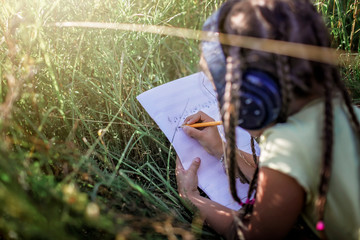 Girl with many braids and headphones listening music and writing music text at flower field