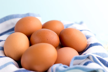 Brown Chicken eggs with rustic cloth on the bright blue background. Farm natural products, food or Easter concept