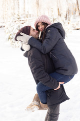 Young hipster couple hugging each other on winter vacation in snowy forest